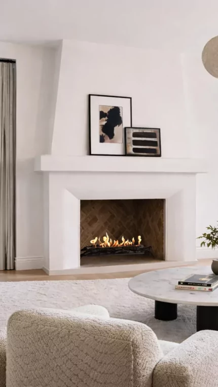 EcoSmart Fire Heritage 50 Grate installed in a white built-in fireplace with visible flame, set in a bright contemporary living room featuring a curved sofa, marble coffee table and large black-framed windows.